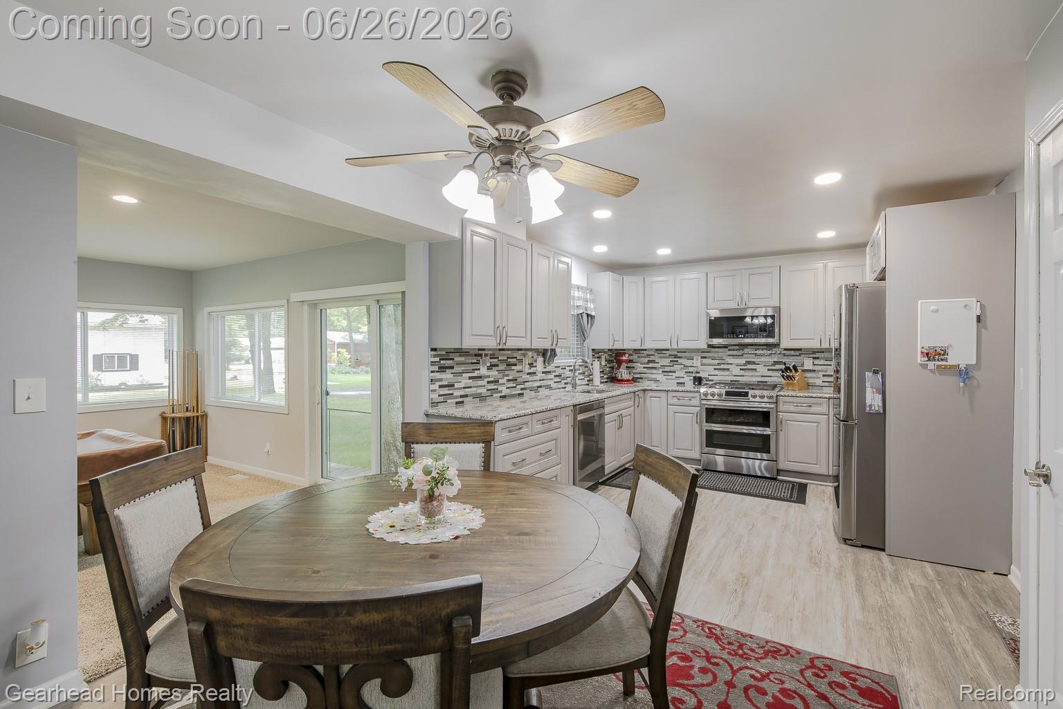 Kitchen featuring light-toned cabinetry, stainless steel appliances, mosaic tile backsplash, and wood-finish flooring