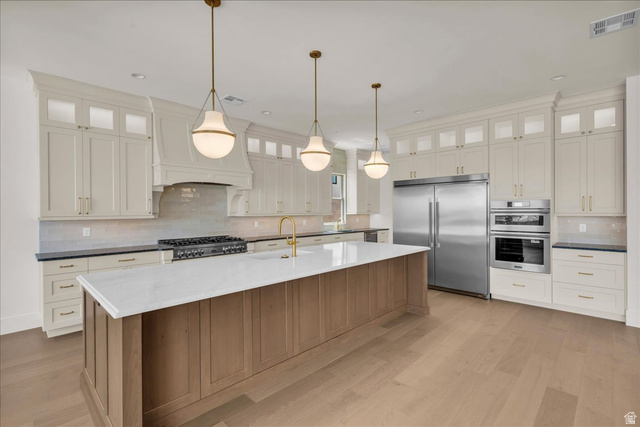 1620 Belayer Drive St. George, UT 84770 - Photo 11 of 51 Gourmet kitchen featuring a large central island with a light wood-finish base and white countertop, stainless steel appliances, extensive white cabinetry with glass-front uppers, a gas range, and wood-finish flooring