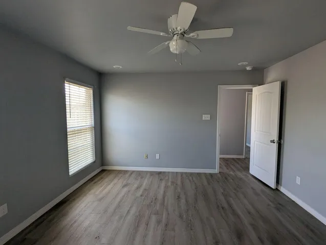 an empty room with wooden floor ceiling fan and windows