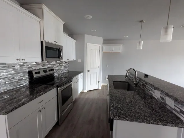 a kitchen with granite countertop a sink dishwasher stove and oven with wooden floor