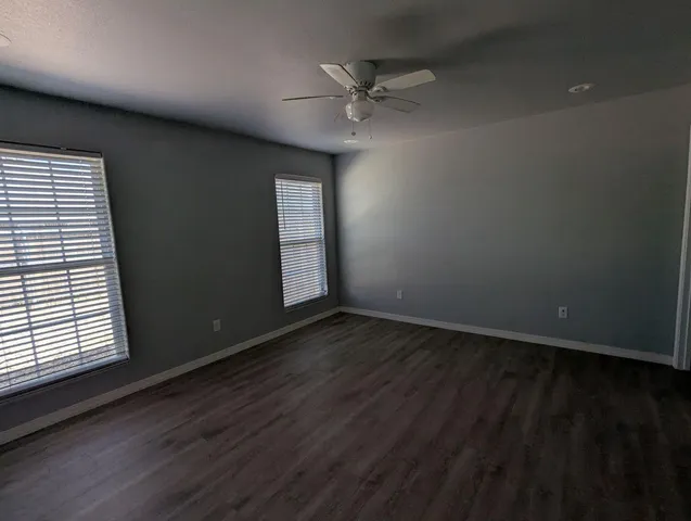 an empty room with wooden floor fan and windows