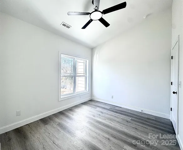 an empty room with wooden floor ceiling fan and windows
