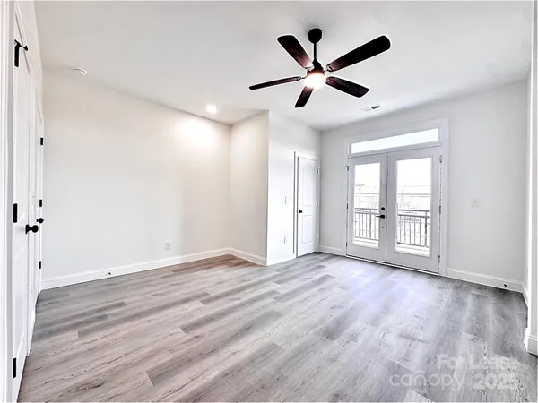 a view of an empty room with wooden floor and a ceiling fan