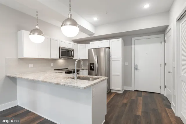 a kitchen with stainless steel appliances granite countertop a refrigerator a sink dishwasher a stove and white cabinets with wooden floor