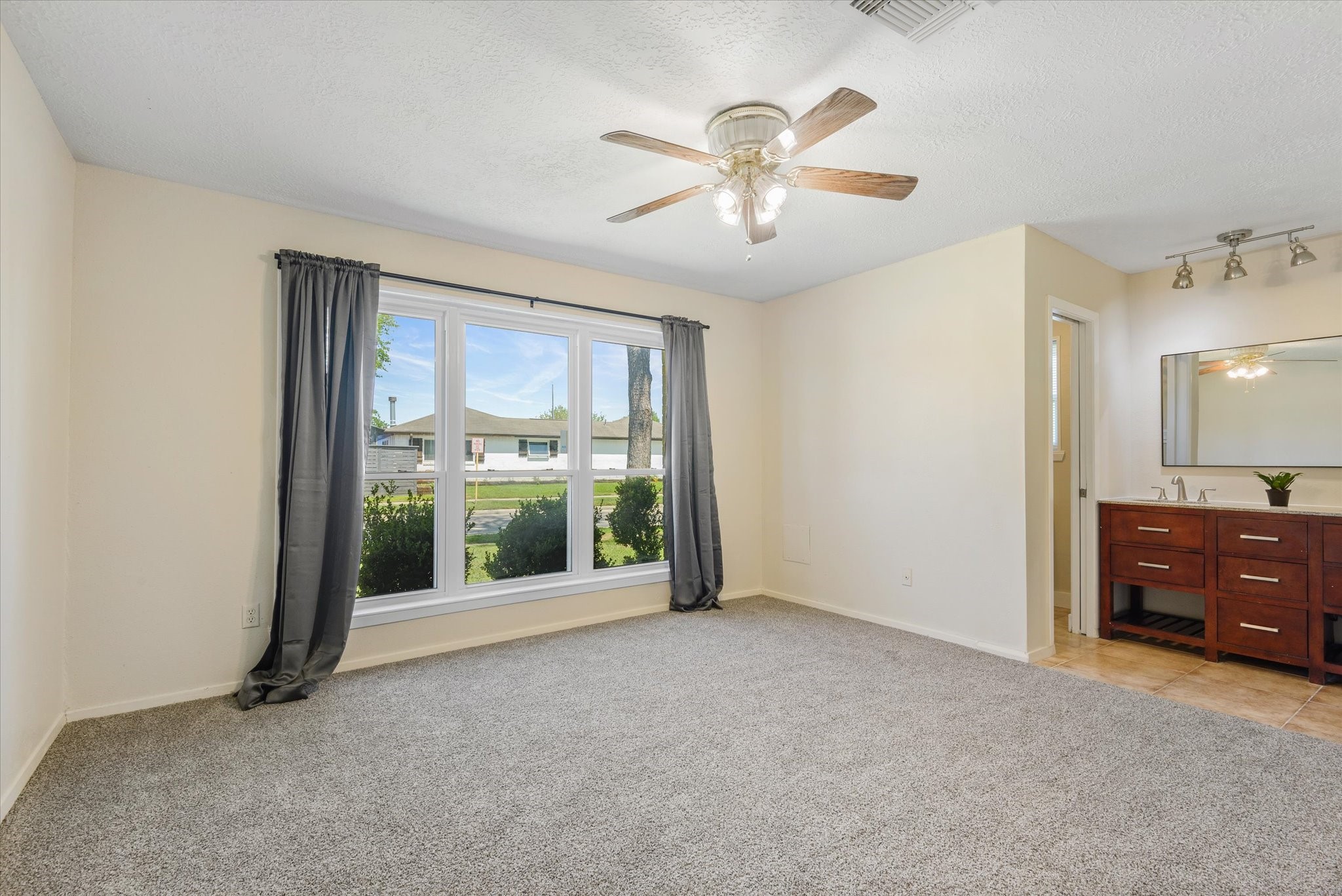 2507 Kings Chapel Road Friendswood, TX 77546 - Photo 11 of 28 Step into the spacious primary suite featuring plush carpet, neutral tones, and a large front-facing window that fills the room with natural light. The layout offers plenty of space for larger furniture and provides easy access to the en suite bath.