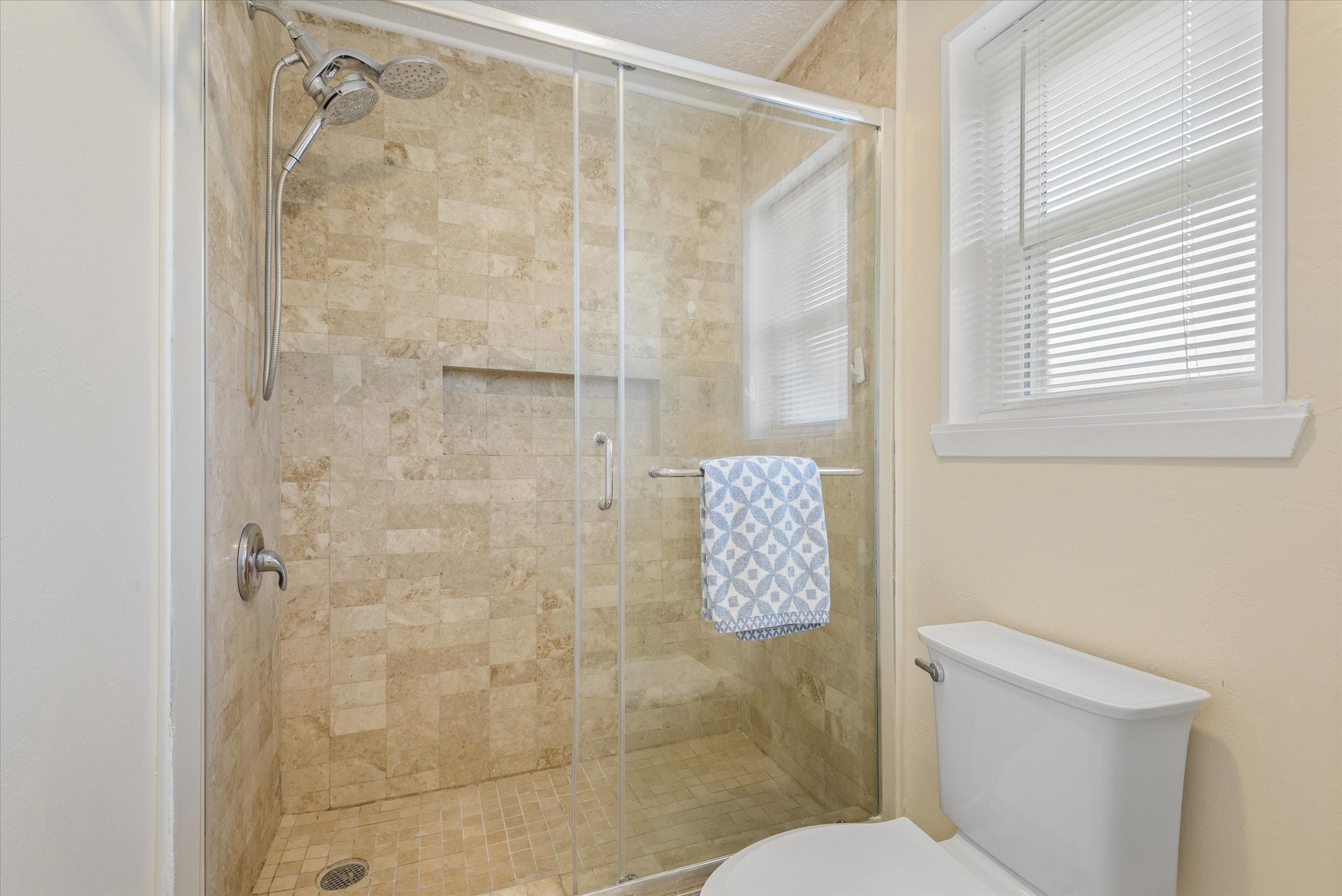 2507 Kings Chapel Road Friendswood, TX 77546 - Photo 13 of 28 The wet room of the primary bath offers an oversized walk-in shower with full tile surround, a built-in niche, and a glass enclosure. A nearby window brings in natural light, giving the space a clean and open feel.
