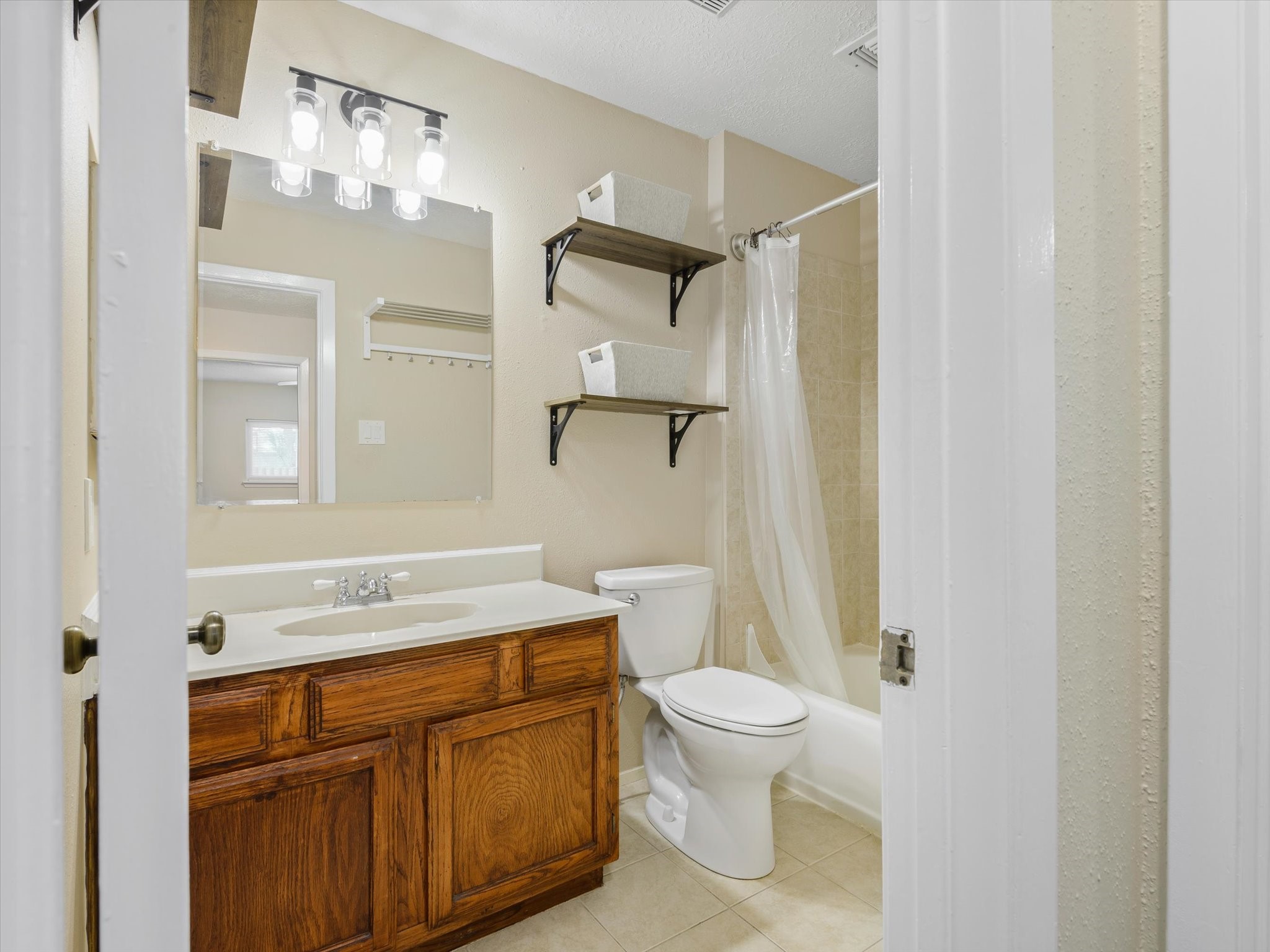 2507 Kings Chapel Road Friendswood, TX 77546 - Photo 16 of 28 The secondary bathroom includes a single sink vanity with storage below, updated lighting, and open shelving for added convenience. A full tub and shower combo completes the space with a clean, simple layout.