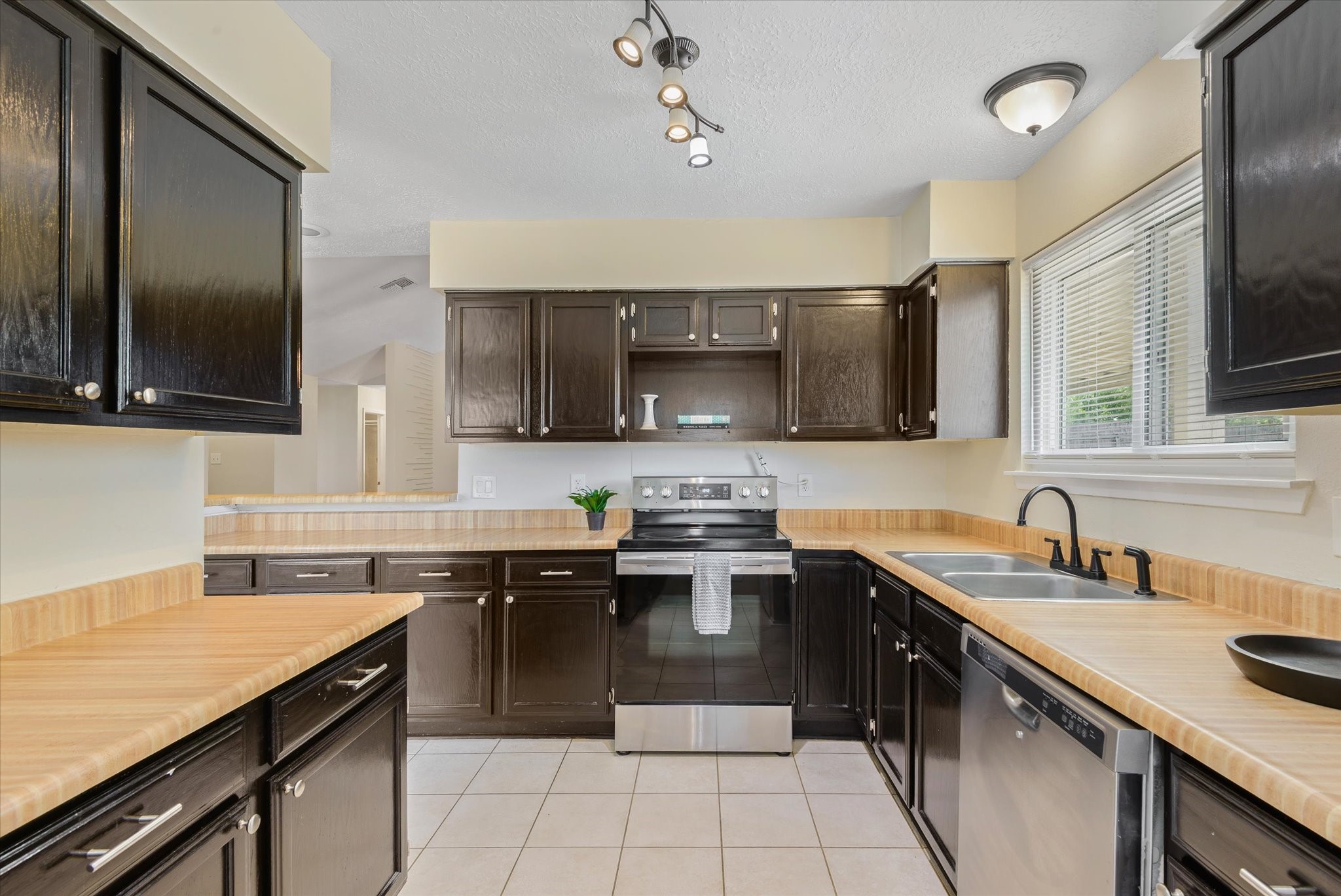 2507 Kings Chapel Road Friendswood, TX 77546 - Photo 7 of 28 The galley kitchen features black cabinetry, generous counter space, and updated appliances, all arranged for easy flow. A pass-through opening connects to the living area, keeping the space open while still maintaining definition.