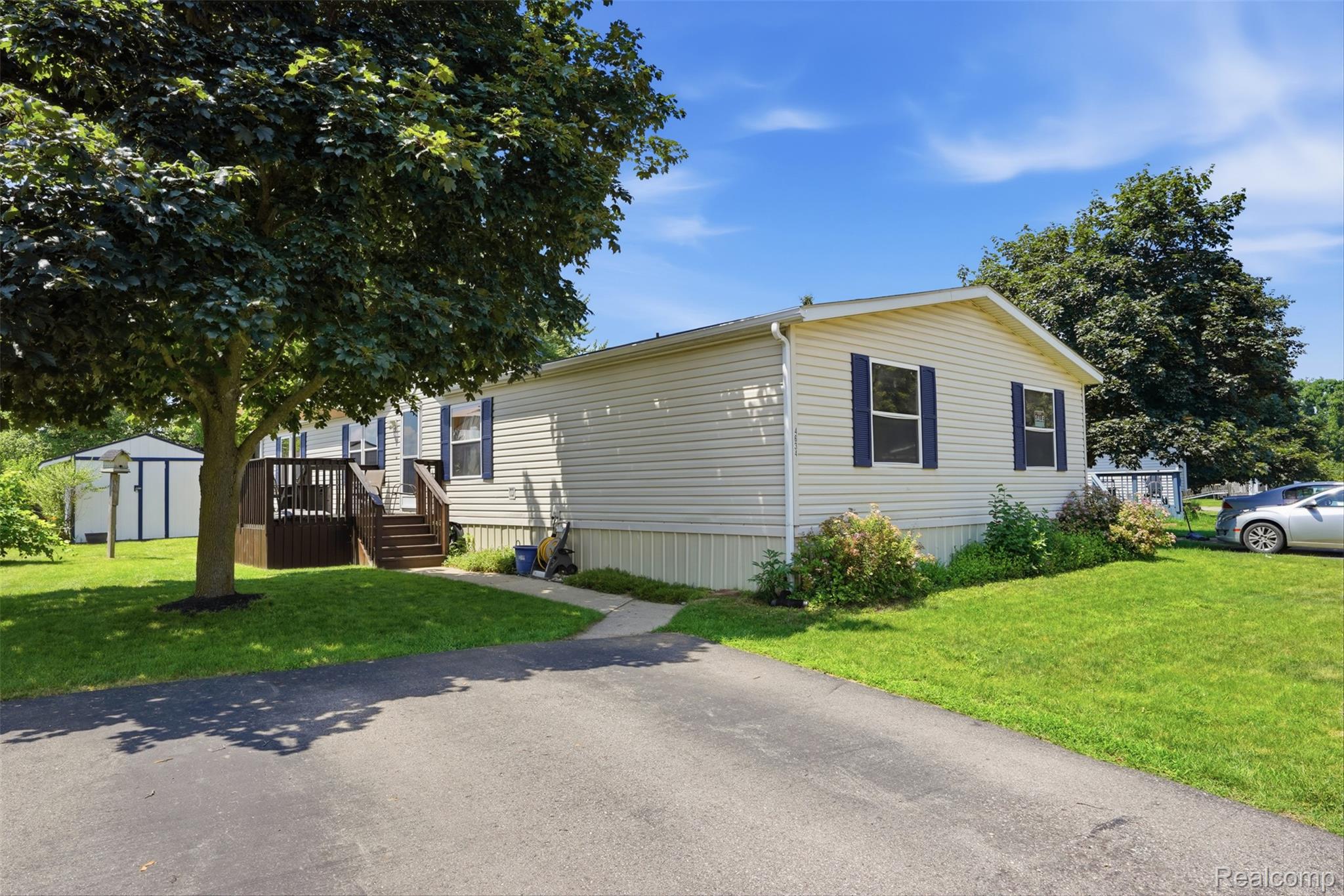 4634 Butternut Street Clarkston, MI 48348 - Photo 2 of 28 Cream-colored siding exterior with blue window shutters, featuring a dark wood deck and stairs