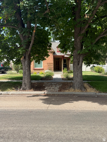 541 300 North Provo, UT 84606 - Photo 4 of 36 Brick exterior residence framed by mature trees, featuring a gabled roofline with dormers, a covered front porch, and a concrete walkway