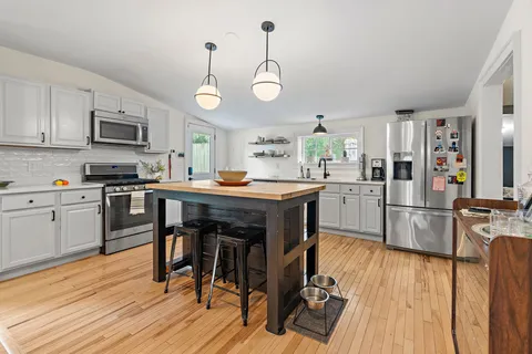 a kitchen with stainless steel appliances granite countertop wooden floors stove and white cabinets
