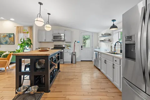 a kitchen with stainless steel appliances kitchen island granite countertop a stove a refrigerator a sink dishwasher and white cabinets with wooden floor