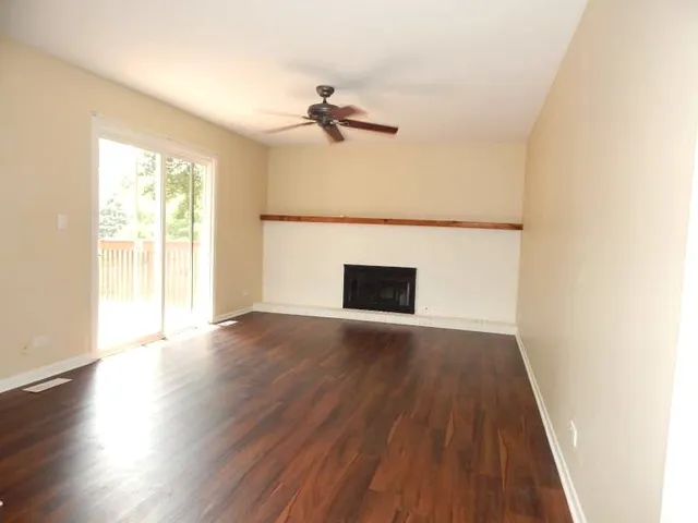 an empty room with wooden floor fan and windows