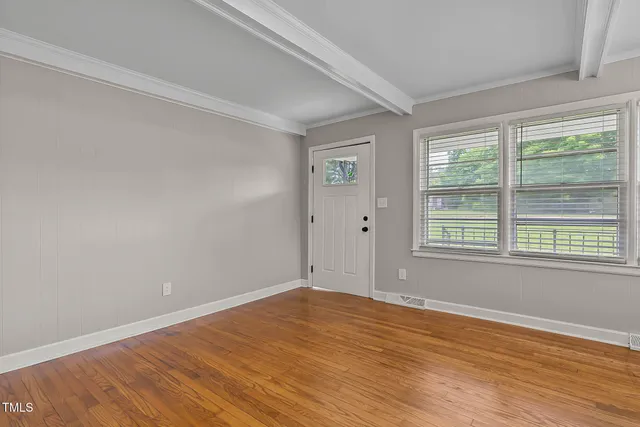 a view of an empty room with wooden floor and a window