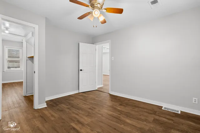 an empty room with wooden floor chandelier fan and windows