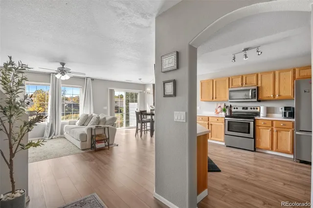 a living room with stainless steel appliances furniture wooden floor and a kitchen view
