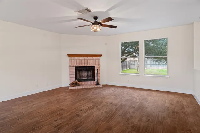 a view of an empty room with wooden floor fireplace and a window