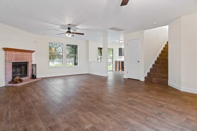 an empty room with wooden floor chandelier fan and windows