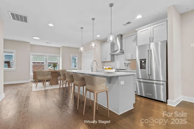 a kitchen with stainless steel appliances granite countertop a refrigerator a sink a stove a dining table and chairs with wooden floor