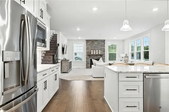 a large kitchen with stainless steel appliances kitchen island granite countertop a refrigerator a oven a stove and white cabinets with wooden floor