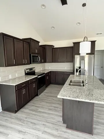 a kitchen with stainless steel appliances granite countertop a stove a sink dishwasher and a refrigerator with wooden cabinets