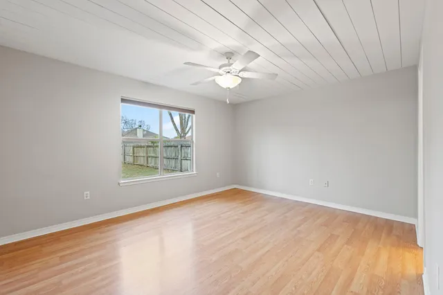 an empty room with wooden floor fan and windows