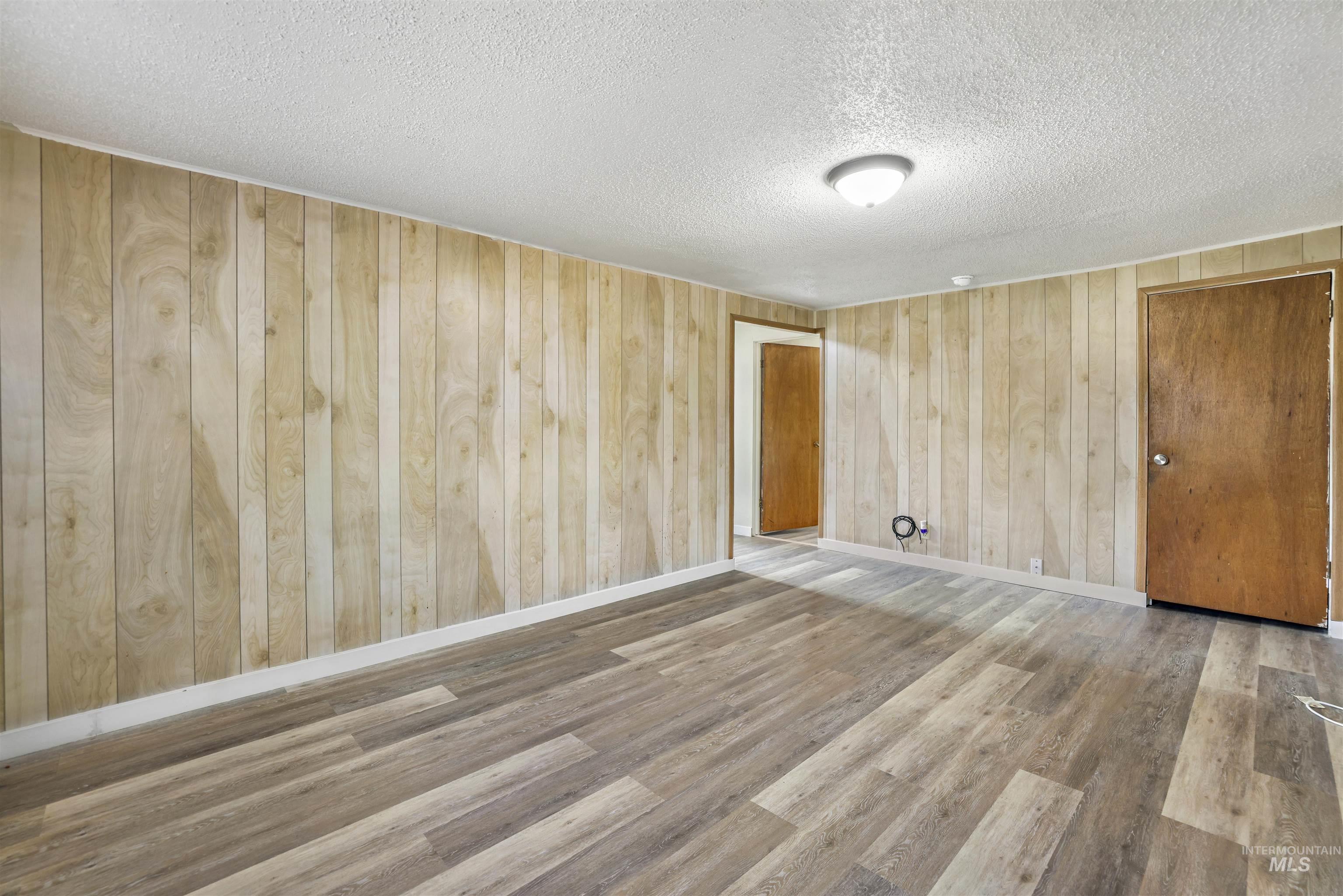 545 Madison Street Twin Falls, ID 83301 - Photo 9 of 23 Unfurnished room featuring wood walls, light wood-style floors, and a textured ceiling