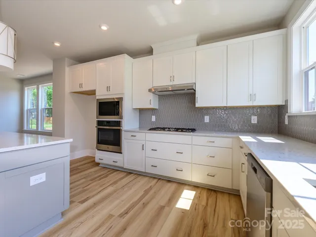 a kitchen with kitchen island granite countertop white cabinets and white appliances with wooden floor