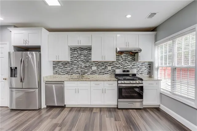 a kitchen with stainless steel appliances a stove a sink dishwasher a refrigerator and white cabinets with wooden floor