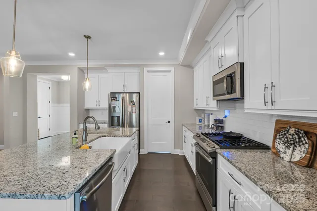 a kitchen with stainless steel appliances granite countertop a stove top oven a sink a dining table and chairs with wooden floor