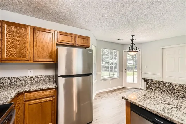 a kitchen with granite countertop stainless steel appliances a refrigerator cabinets and wooden floor