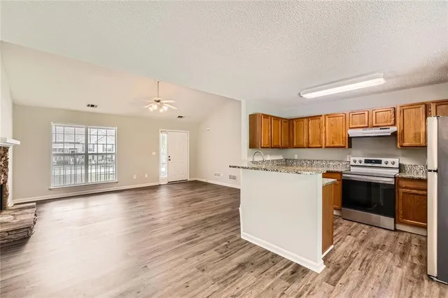 a kitchen with stainless steel appliances granite countertop a stove top oven a sink dishwasher and a refrigerator with wooden floor