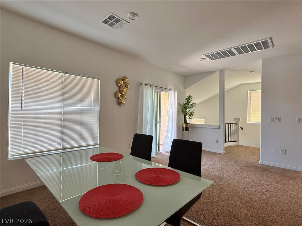 7777 South Westwind Road Las Vegas, NV 89139 - Photo 39 of 46 A dining area flows seamlessly into the living space, featuring neutral carpeting and a modern glass-top table.