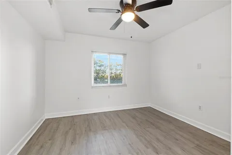 an empty room with wooden floor ceiling fan and window