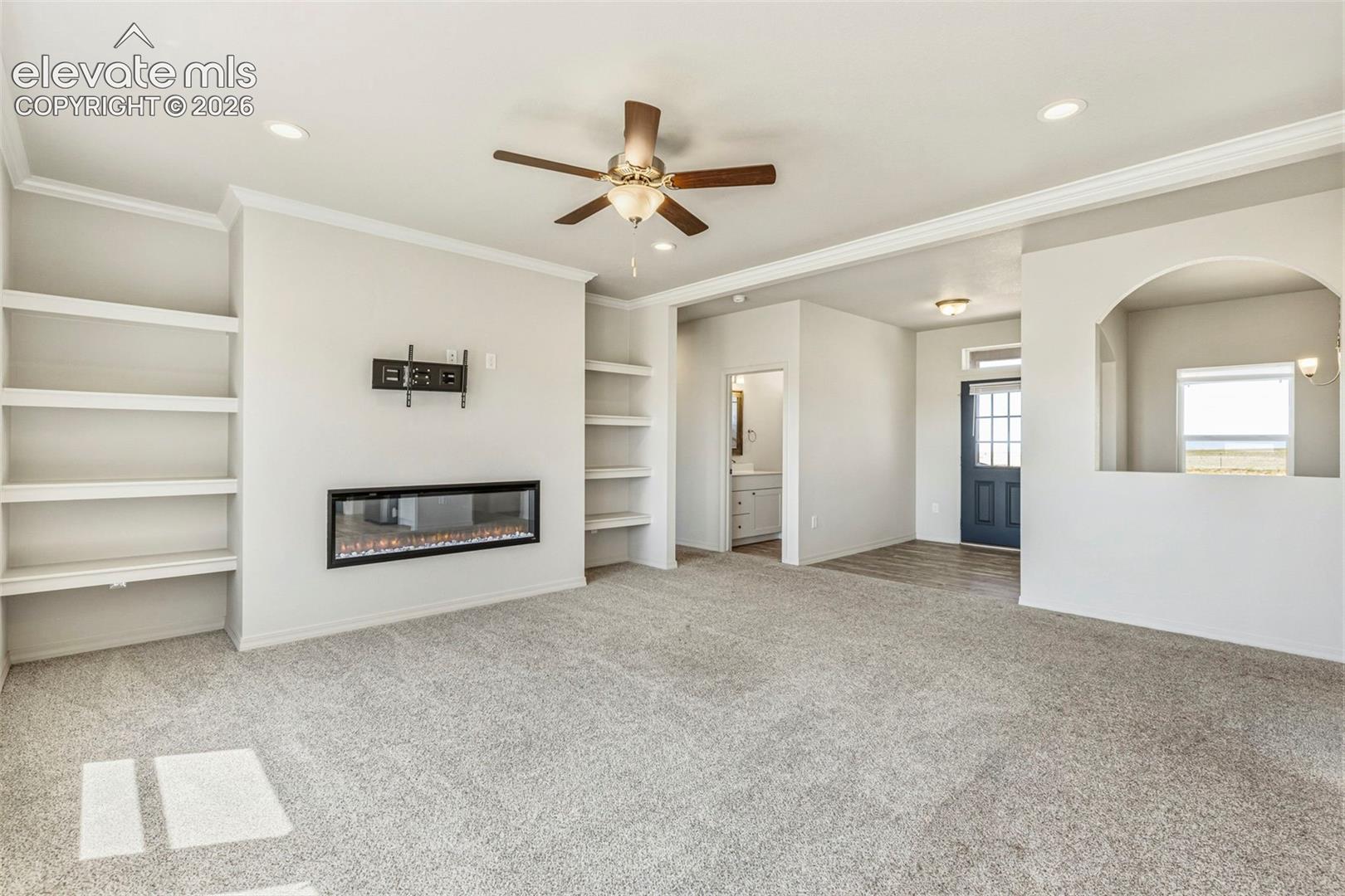 3955 North Yoder Road Yoder, CO 80864 - Photo 10 of 38 Spacious living area featuring an electric fireplace with a wall-mounted television bracket, built-in shelving, recessed lighting, and a ceiling fan