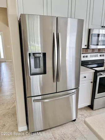 a view of a refrigerator in kitchen and an empty room