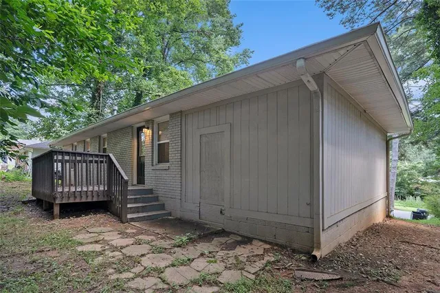 a view of a small house with wooden fence and large trees
