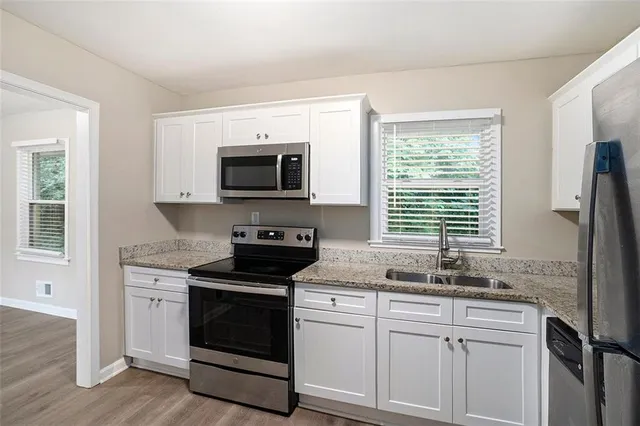 a kitchen with granite countertop white cabinets and a stove with wooden floor