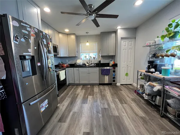 a kitchen with stainless steel appliances granite countertop a refrigerator a sink dishwasher a stove a dining table and chairs with wooden floor