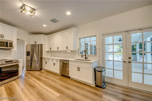 a large kitchen with stainless steel appliances granite countertop a stove a sink dishwasher a refrigerator and a dining table with wooden floor