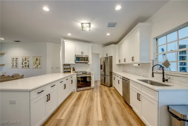 a large white kitchen with stainless steel appliances granite countertop a sink dishwasher a stove and a refrigerator with wooden floor