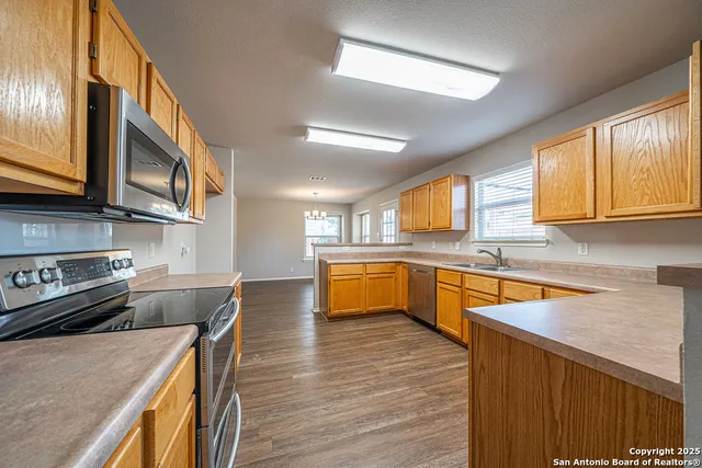 a kitchen with stainless steel appliances granite countertop wooden cabinets a sink dishwasher a stove and a refrigerator with wooden floor