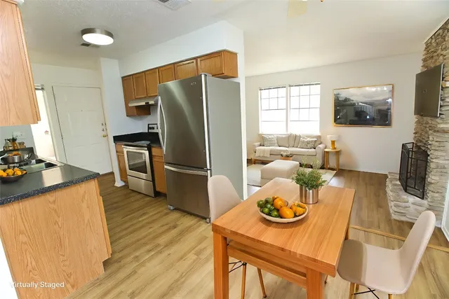 a kitchen with stainless steel appliances granite countertop a refrigerator a stove a sink a dining table and chairs with wooden floor