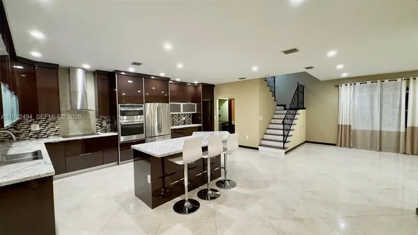 a kitchen with stainless steel appliances kitchen island granite countertop a refrigerator a sink a stove a dining table and chairs with wooden floor