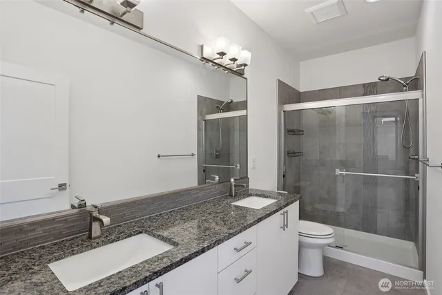 a bathroom with a granite countertop sink a toilet a mirror and shower