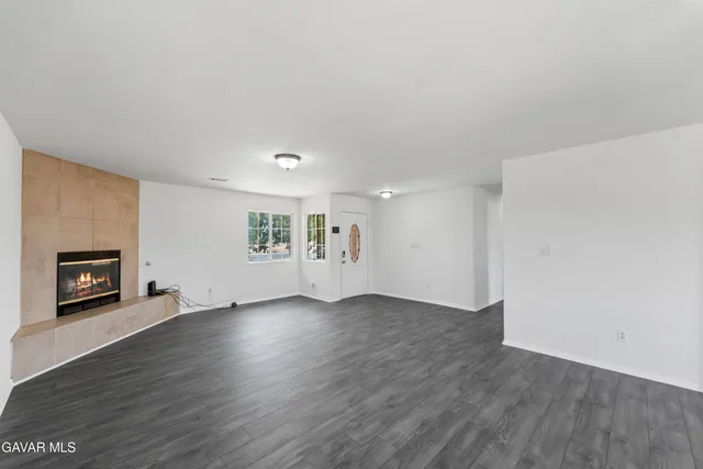 an empty room with wooden floor fire place and windows