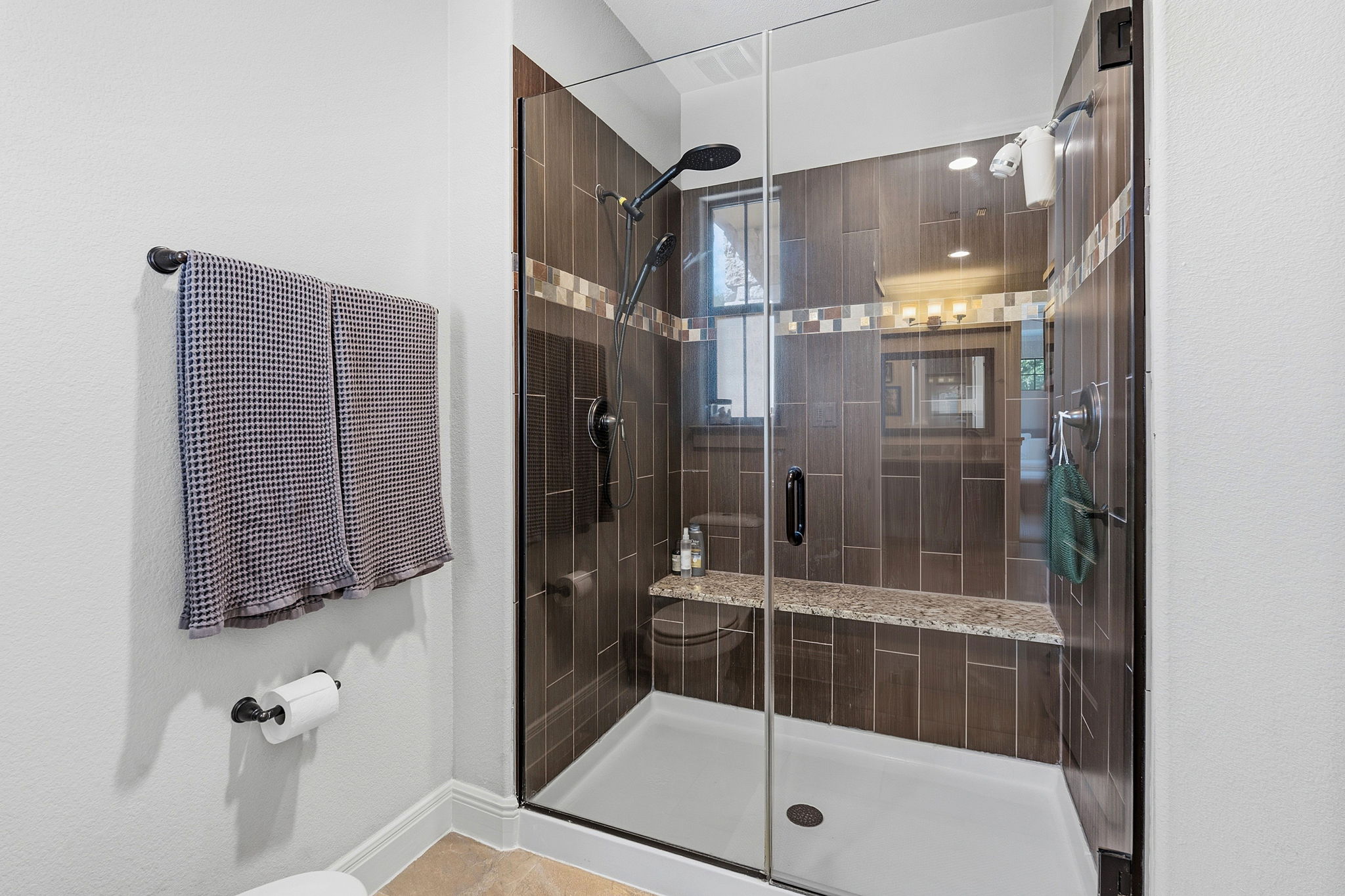 15317 Falconhead Grove Loop Austin, TX 78738 - Photo 18 of 36 Glass-enclosed shower with dark brown tile surround and decorative accent band