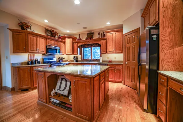 a kitchen with stainless steel appliances granite countertop a refrigerator a sink dishwasher a stove and a dining table with wooden floor