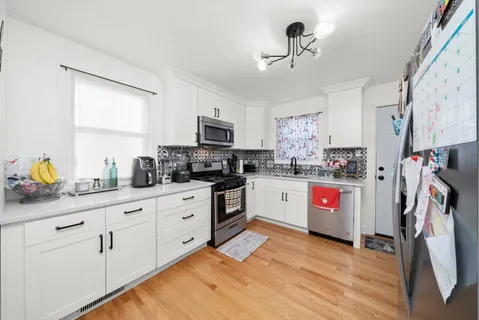 a kitchen with stainless steel appliances granite countertop a refrigerator a stove top oven a sink dishwasher and white cabinets with wooden floor