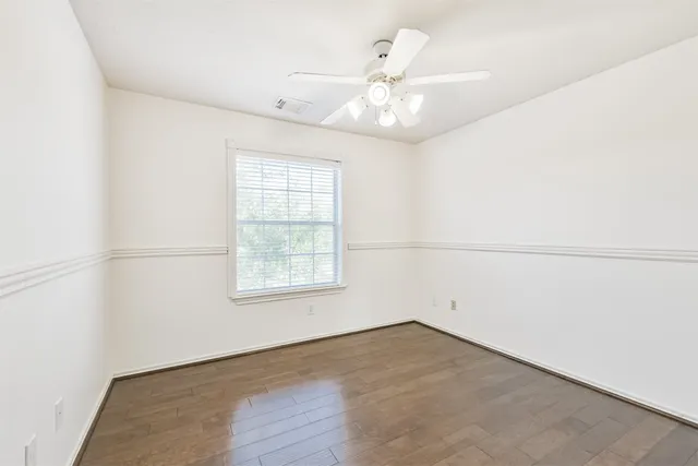 an empty room with chandelier fan and windows